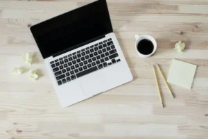 A laptop on a wooden table with a cup of coffee and a notepad, perfect for studying STEM Education or IIT JEE Mains.
