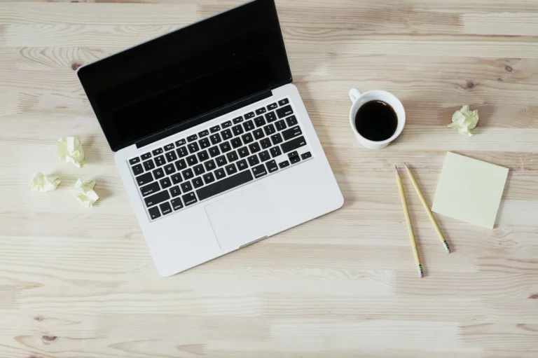 A laptop on a wooden table with a cup of coffee and a notepad, perfect for studying STEM Education or IIT JEE Mains.