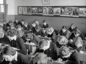 A black and white photo of a classroom with many students sitting at desks.